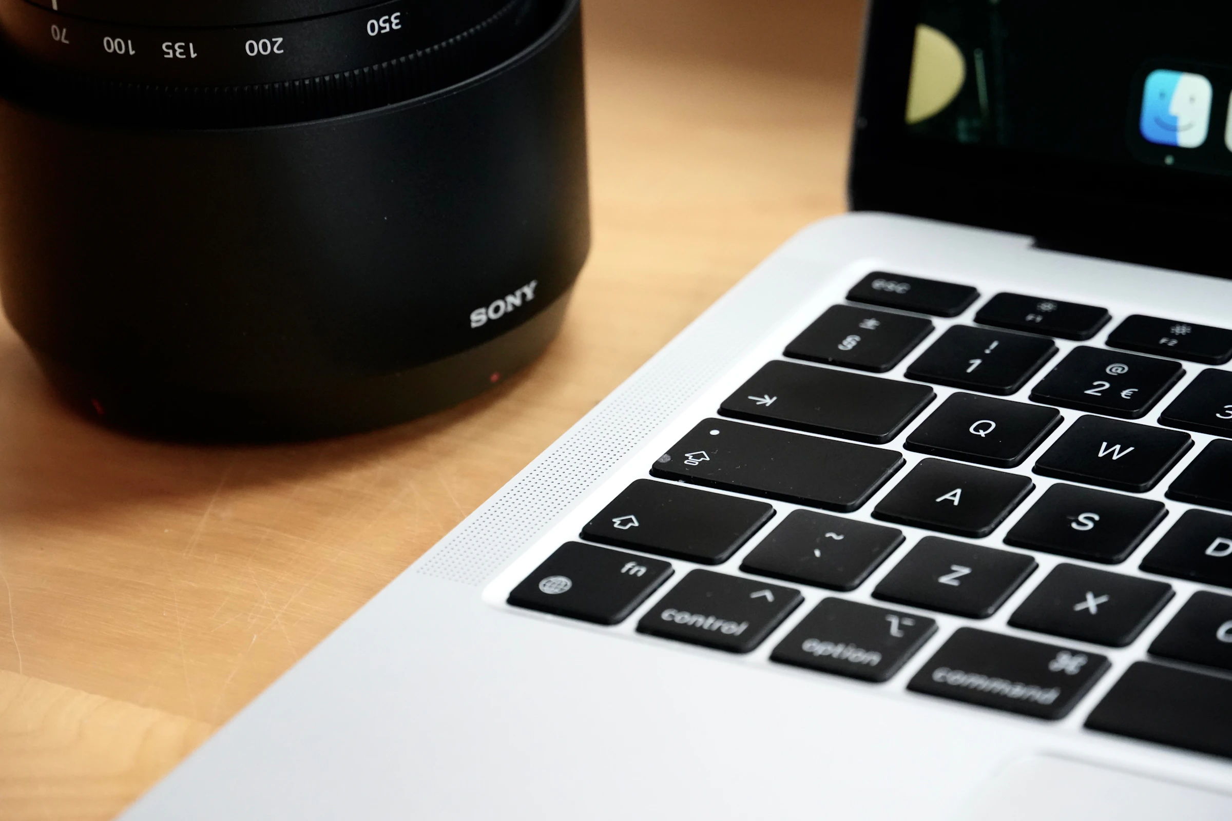 A camera lens beside a laptop on a working photographer’s desk